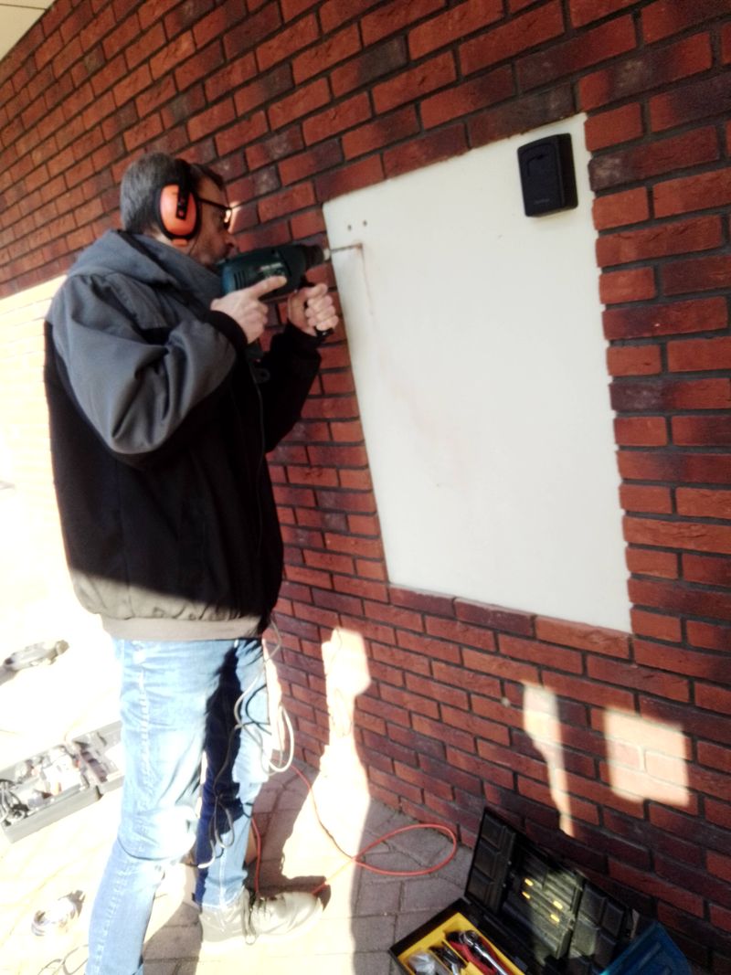 Jeroen boort een sleutelkastje in een bakstenen buitenmuur